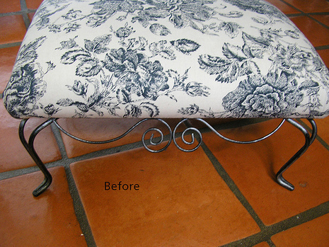 A metal foot stool with a grey floral covering is on a red tile floor.