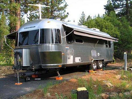 Airstream trailer parked an asphalt in a wooded area.