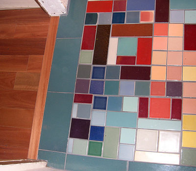 Floor with different sized multi colored tiles next to a wood floor.