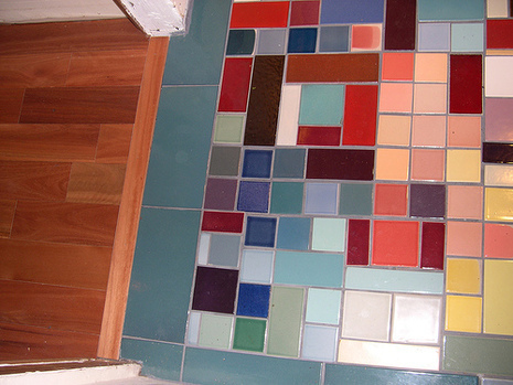 Floor with different sized multi colored tiles next to a wood floor.