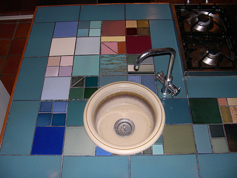 Kitchen counter top is designed with colorful tiles near to stove and sink.