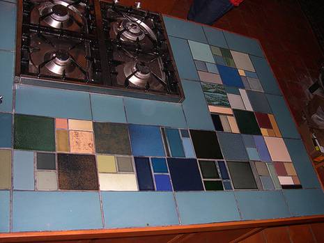 Kitchen counter top near gas stove is designed with colorful tiles.