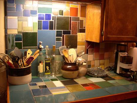 The multicored tile kitchen counter and backsplash with containers of kitchen utensils on it.