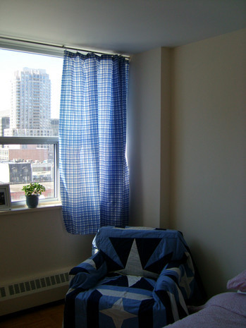 A blue, black and white chair is in the corner of a room with a blue curtain.