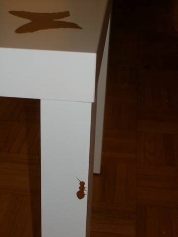 The corner of a table with a painting of a bug crawling up one of its legs.