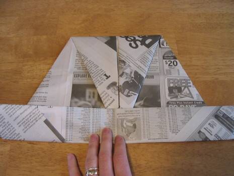 A person is folding a piece of newspaper.