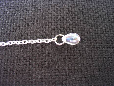 A chain with a bead are on a grey fabric.