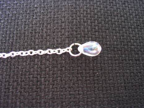 A chain with a bead are on a grey fabric.