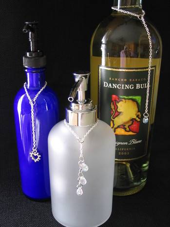 Three bottles of different colors and sizes wearing decorative bottle necklaces around their necks.