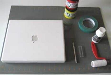 White Macbook on a grey mat with tape, a roller, and paint next to it.