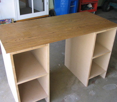 A partical board desk with shelves on each side in a garage.