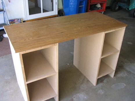 A partical board desk with shelves on each side in a garage.