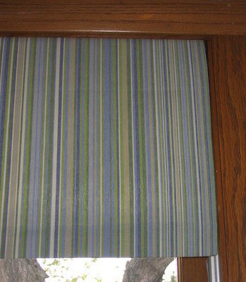 Blue and green lined window treatment on a window with wood trim around its border.