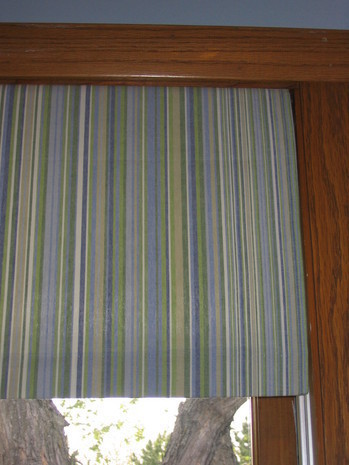 Blue and green lined window treatment on a window with wood trim around its border.