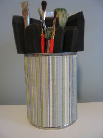A striped multi-colored tin can with paintbrushed inside it.