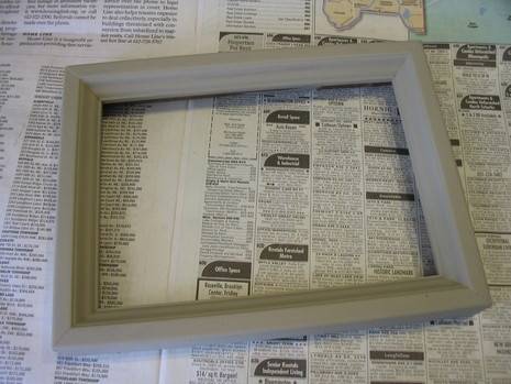A freshly painted grey picture frame rests on some newspaper.