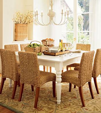 Basket of produce next to serving tray on top of white dining room table next to group of chairs in a dining room.