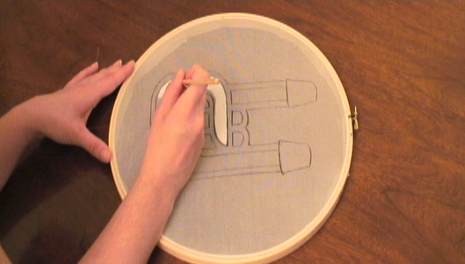 A person uses a pencil to outline a design to be printed on a piece of fabric wrapped around an embroidery hoop.