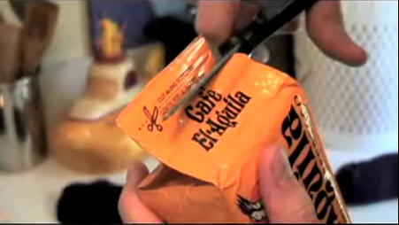 Person cutting cafe el-aguila packet with scissor.