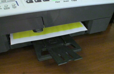 A printer sitting on a wooden desk in the process of printing a colored print.
