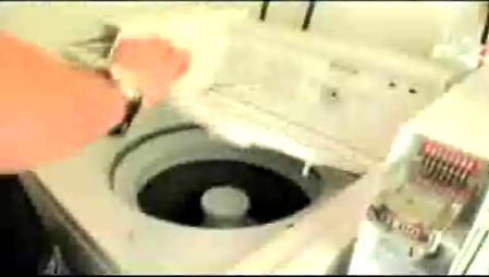 A persons arm opening the top of a coin-op washing machine.