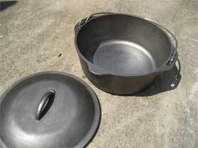 A cast iron pot sits on the ground next to its lid.