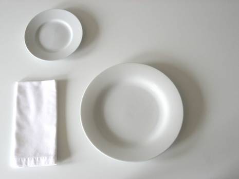 A small white plate, a large white plate, and a folded white napkin sit on a white surface.