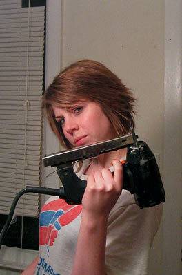 A woman holding up a nail gun in her left hand.