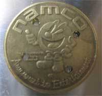 A gold Namco Pacman coin has four holes drilled in it.