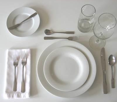 An entire place setting consisting of white plates and a saucer, two glasses, three forks, two knives, and two spoons.