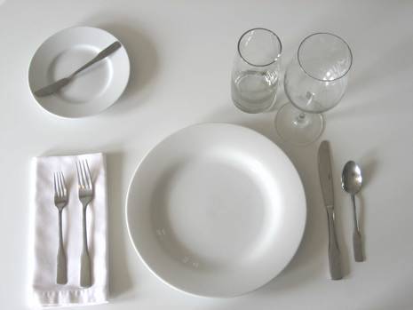 White plate next to two glasses, a plate with a small fork, two forks on a napkin, and a spoon and a knife.