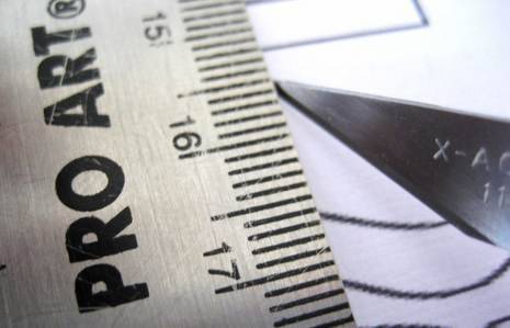 A closeup view of a standard ruler as it lays next to the tip of a craft knife.