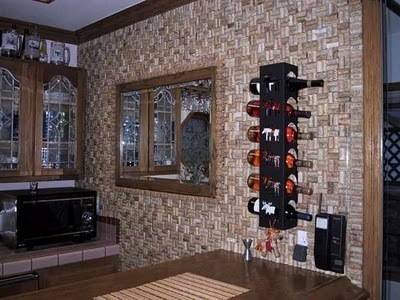 Small wooden dining room with a wooden table pressed up against a wall with wine bottles hanging on a rack above it.
