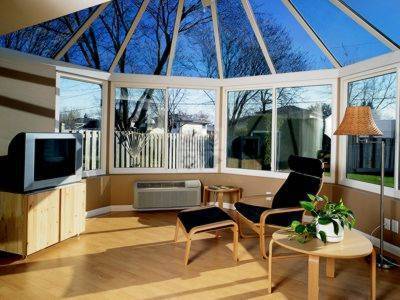 Room with glass walls, T. V., chair, stool, table with potted plant and glass roof.