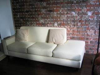 A white sofa sits in a room with brick wall.
