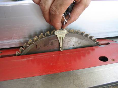 A hand holding a key next to the the saw blade on a red table saw.