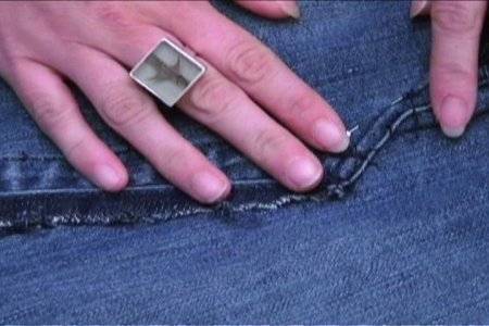 A person wearing a ring holds a seam on their jeans with their fingers.