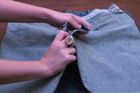 Ringed fingers opening a zip in the jeans pant.