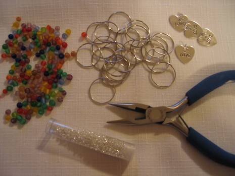 Several jewelry beads and rings are next to pliers.