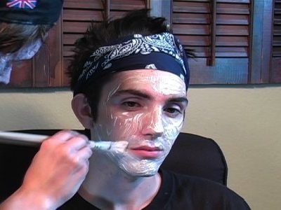 A young man has white paint applied to his face with a paintbrush.