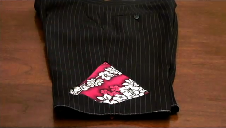 A pair of black shorts with pinstripes and a square Hawaaian floral print patch on it.