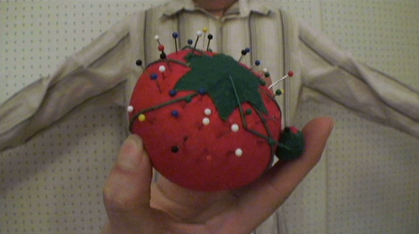 Pincushion with a a variety of pins in front of a white striped shirt.