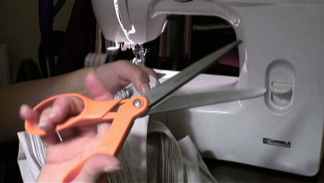 A person is cutting cloth with a scissor and the person is in front of a sewing machine.