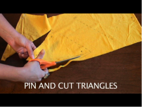 A hand cutting triangles out of a piece of yellow cloth with orange scissors.