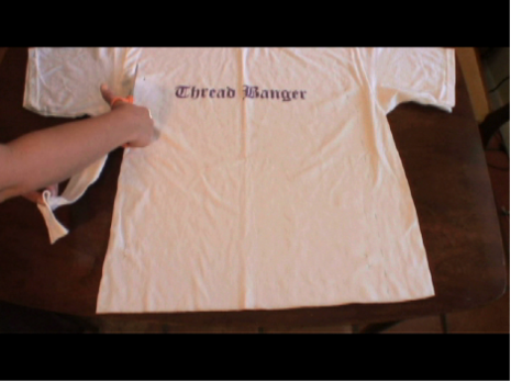 A hand holding a pair of scissors and cutting a T-shirt.