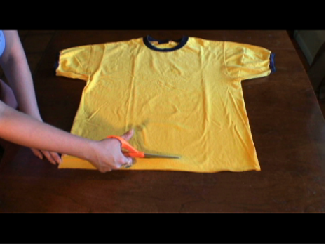 A woman cutting the bottom of a yellow shirt lengthwise.