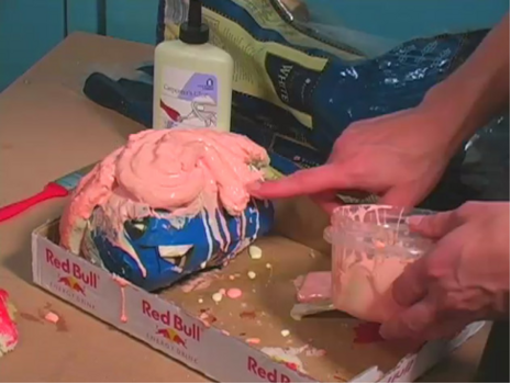 A man fingering a pink slurry mess inside of a cardboard Red Bull case container.