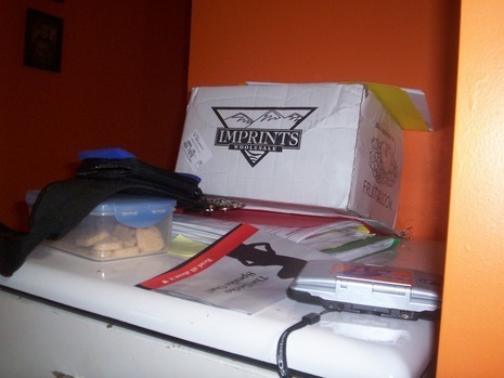 Clutter of things like a cardboard box, plastic container with biscuits, a gadget, a book, files and others.