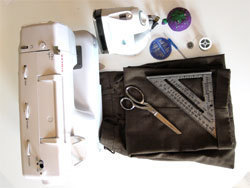 A sewing machine laying on its side, a white iron, a purple ball, a pair of stainless steel scissors and a square layig on a folded piece of dark cloth.