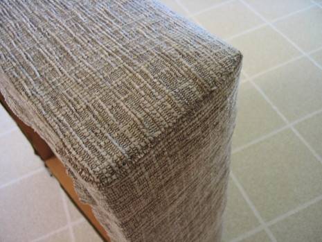 An open bottom on an ottoman turned on its side covered in a beige woven fabric